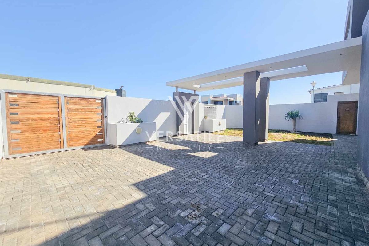 A spacious paved rear courtyard featuring a modern concrete pergola, secure timber gate, and perimeter boundary walls.