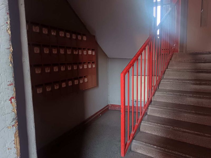 Apartment building entrance lobby featuring a concrete staircase with a red metal handrail and a wall-mounted bank of mailboxes.