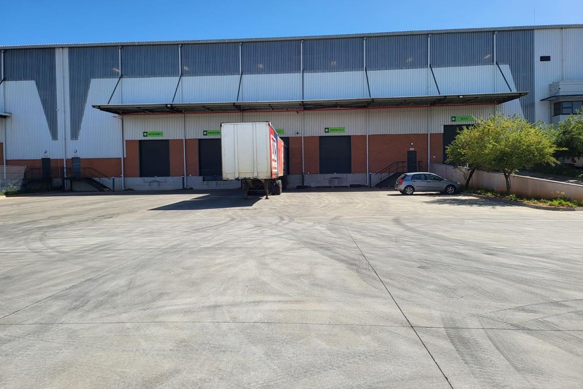 Industrial warehouse exterior featuring multiple loading bays with roller shutter doors and a large concrete yard area for logistics and transport operations.