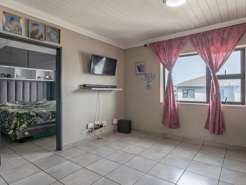 A living room featuring tiled flooring and a tongue and groove ceiling, with a view into the adjacent bedroom.