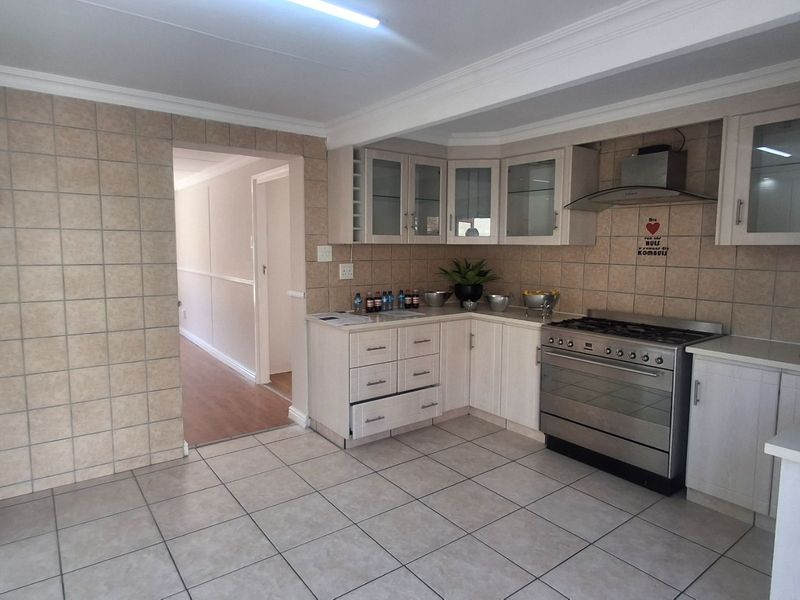 A functional kitchen featuring tiled flooring, neutral cabinetry, a stainless steel gas stove with extractor fan, and a tiled splashback.
