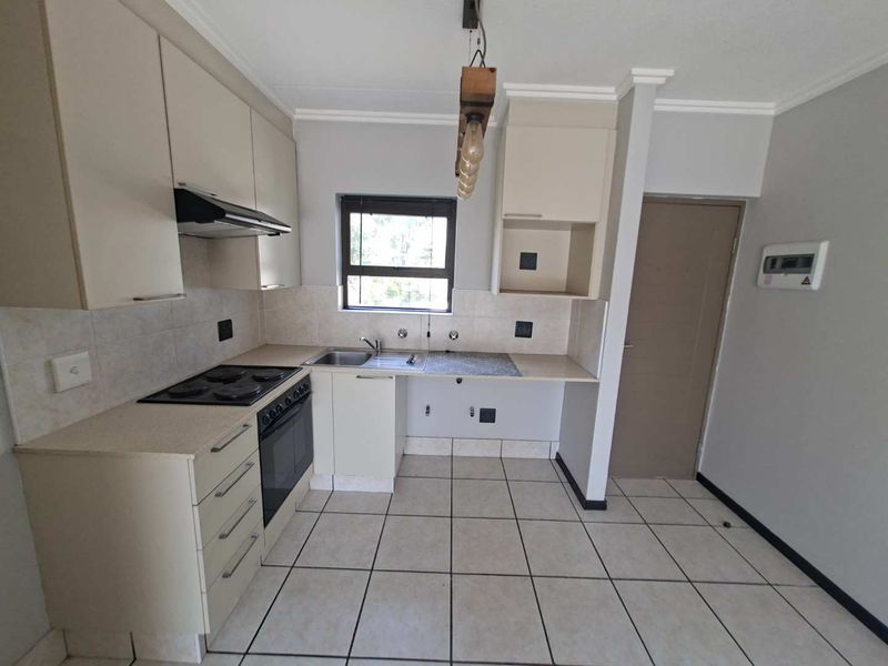 A clean, functional kitchen featuring built-in cabinetry, stone countertops, an electric hob, oven, and extractor fan, with neutral tiled flooring throughout.