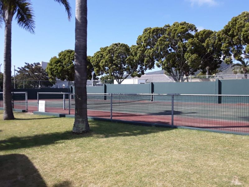 A well-maintained outdoor tennis court facility featuring perimeter fencing and surrounding landscaped lawn areas.
