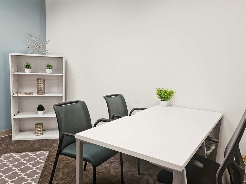 A functional office space featuring neutral wall tones, carpeted flooring, and an integrated electrical outlet, suitable for a professional work environment.