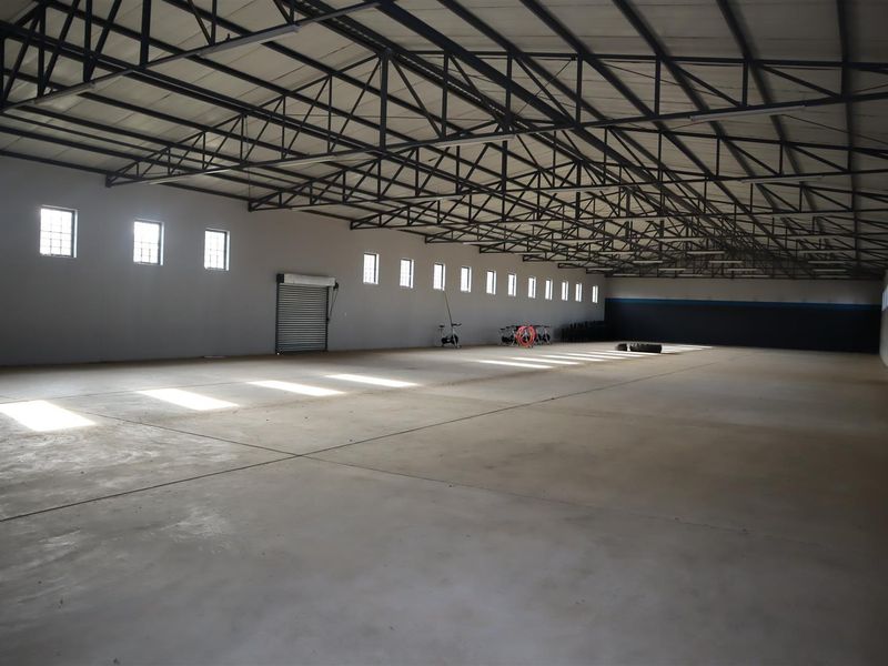A large, open-plan utility or warehouse space featuring exposed steel roof trusses, polished concrete flooring, and multiple windows providing natural light.