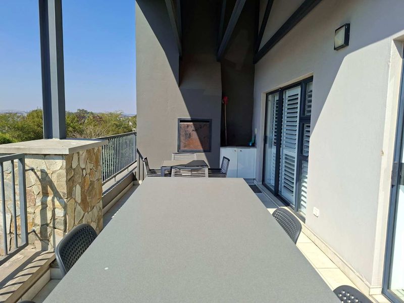 Spacious covered balcony featuring a built-in braai, stone-clad pillar, and sliding door access, offering an ideal outdoor entertainment area with scenic views.