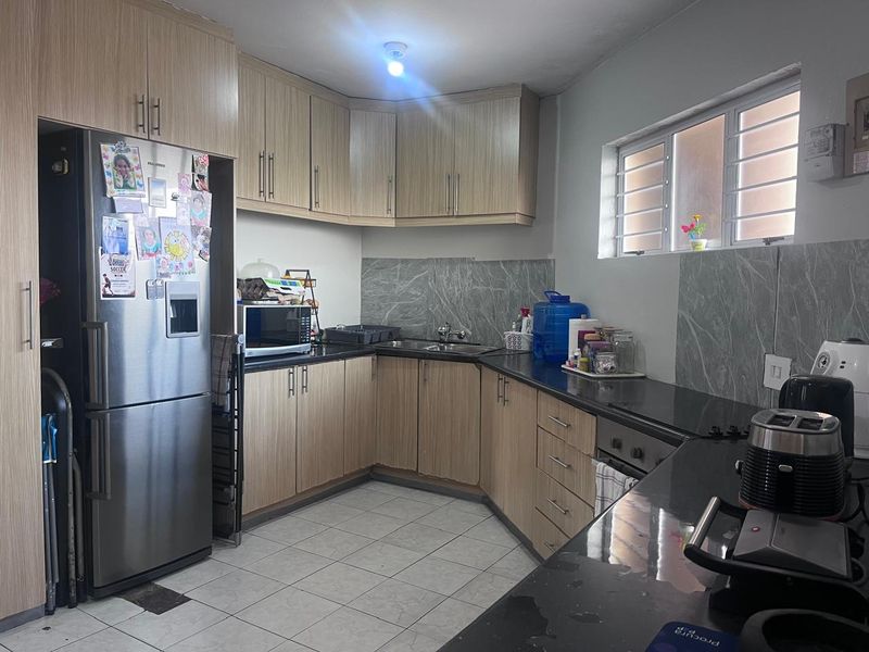 A functional kitchen featuring light wood-look cabinetry, dark granite countertops, marble-effect splashbacks, and ceramic floor tiles with a window for natural light.