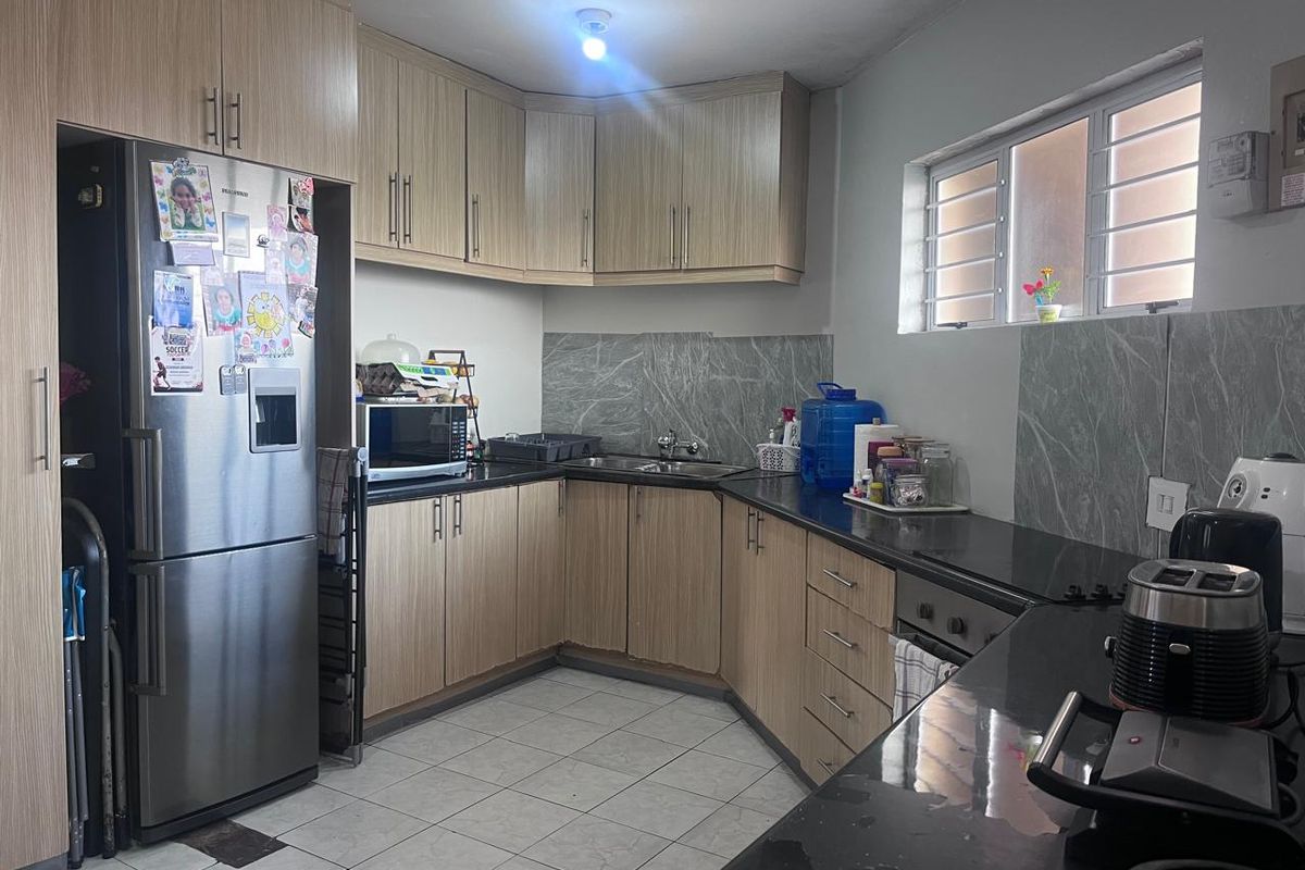 A functional kitchen featuring light wood-look cabinetry, dark granite countertops, marble-effect splashbacks, and ceramic floor tiles with a window for natural light.