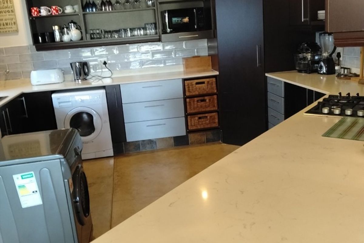 Modern kitchen featuring dark cabinetry, light stone countertops, subway tile backsplash, built-in appliances, and a functional breakfast bar area.