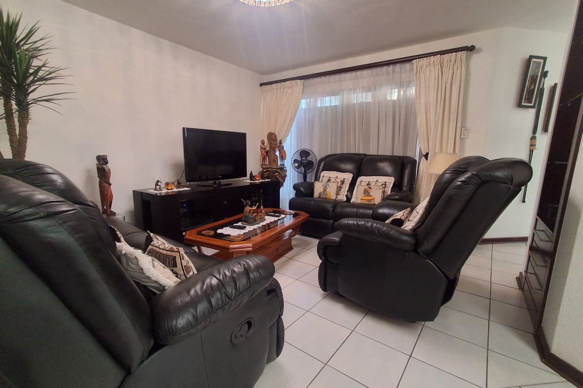 A comfortable living room featuring tiled flooring and large windows with curtain treatments, providing a functional and well-lit space for relaxation.