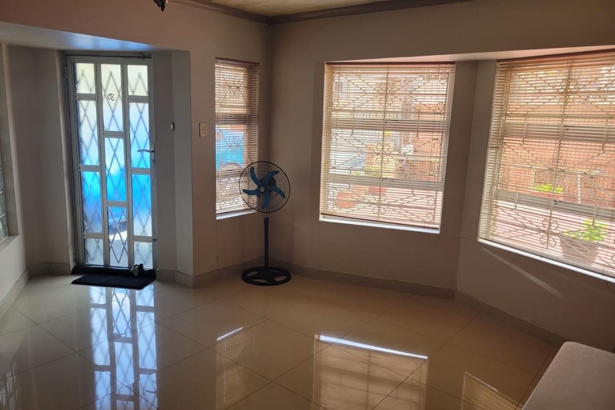 A bright, empty living area featuring polished tiled floors, security gates, and large windows with fitted blinds, offering a clean canvas for interior design.