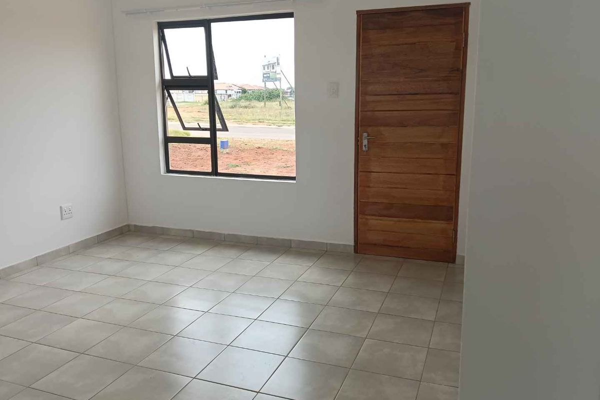 A bright, empty bedroom featuring neutral tiled flooring, a large window with black frames, and a solid wood door.