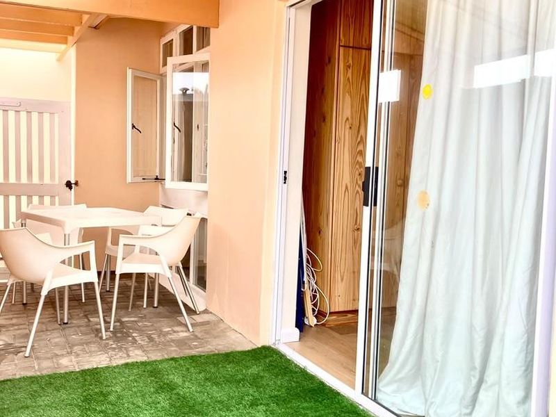 A covered patio area featuring paved flooring, artificial turf, and a sliding glass door providing access to the interior living space.