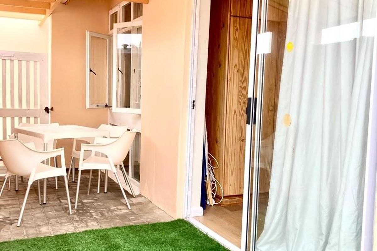A covered patio area featuring paved flooring, artificial turf, and a sliding glass door providing access to the interior living space.