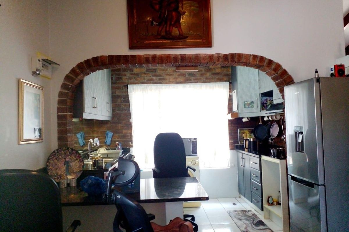 A kitchen area featuring an exposed brick archway, granite countertops, and built-in cabinetry with tiled flooring.