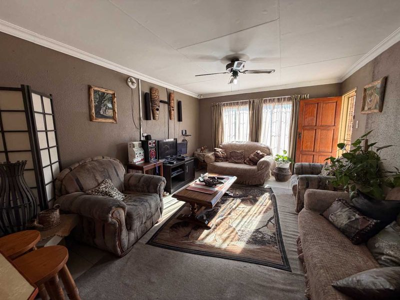 A cozy living room featuring tiled flooring, a ceiling fan, and crown molding, with natural light entering through the window and door.