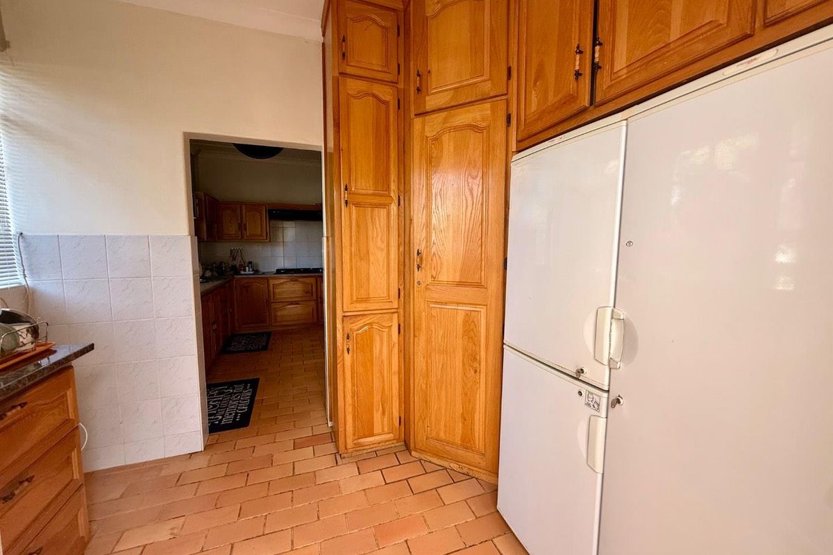 A functional kitchen featuring traditional wooden cabinetry, tiled flooring, and a tiled splashback, offering a classic layout with potential for modern updates.
