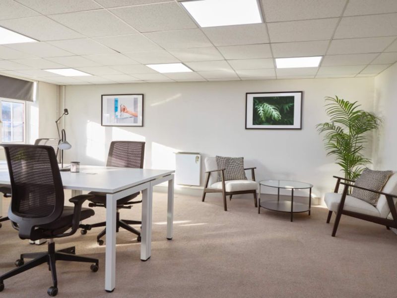 A bright, professional office space featuring a suspended ceiling with recessed lighting, carpeted flooring, and a wall-mounted electric heater.