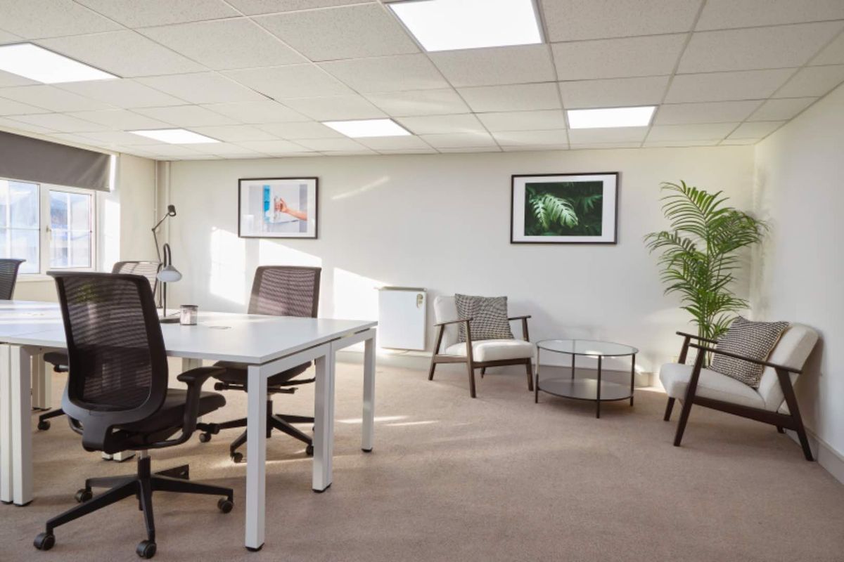 A bright, professional office space featuring a suspended ceiling with recessed lighting, carpeted flooring, and a wall-mounted electric heater.