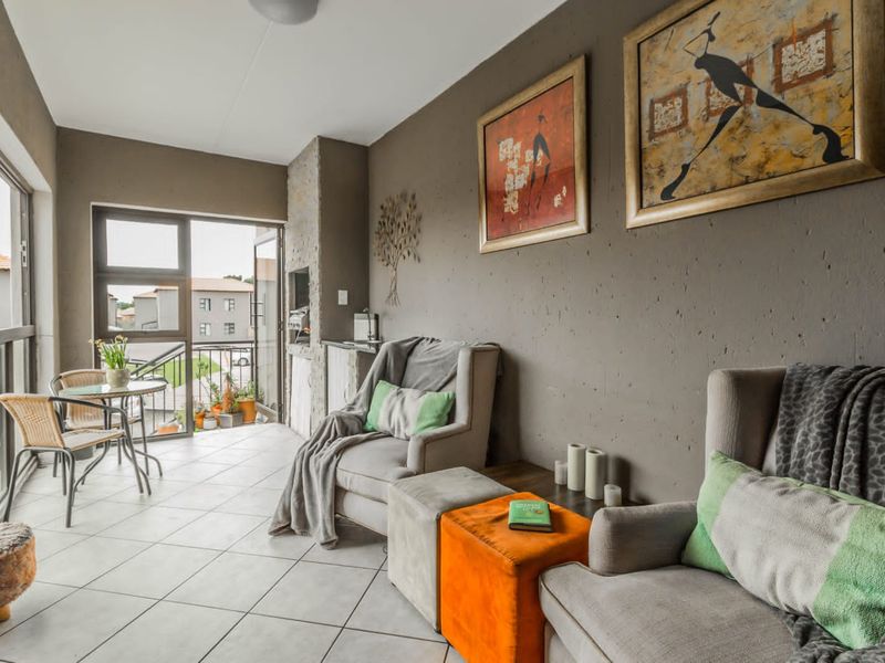 A covered balcony featuring tiled flooring, a built-in braai, and sliding glass doors leading to an outdoor seating area.