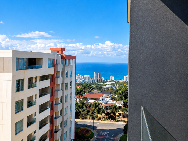 Elevated urban view overlooking the street, surrounding apartment buildings, and the distant ocean horizon from a modern balcony.