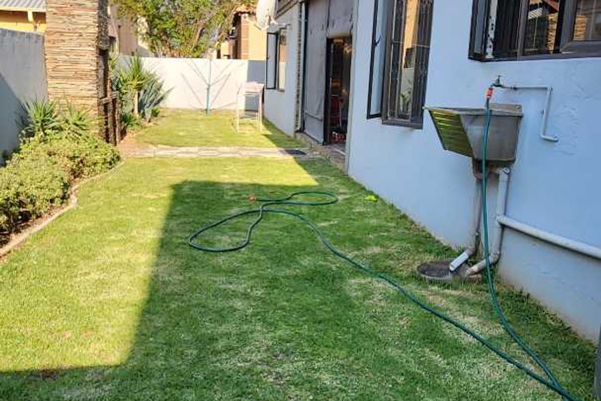 A side garden area featuring a lawn, a built-in brick braai, and an external utility sink attached to the house wall.