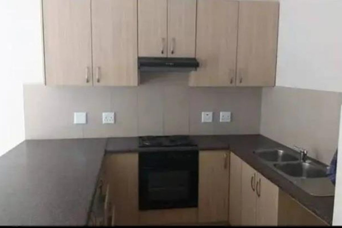 A functional kitchen featuring light wood-finish cabinetry, dark laminate countertops, a built-in oven with hob, and a double stainless steel sink.