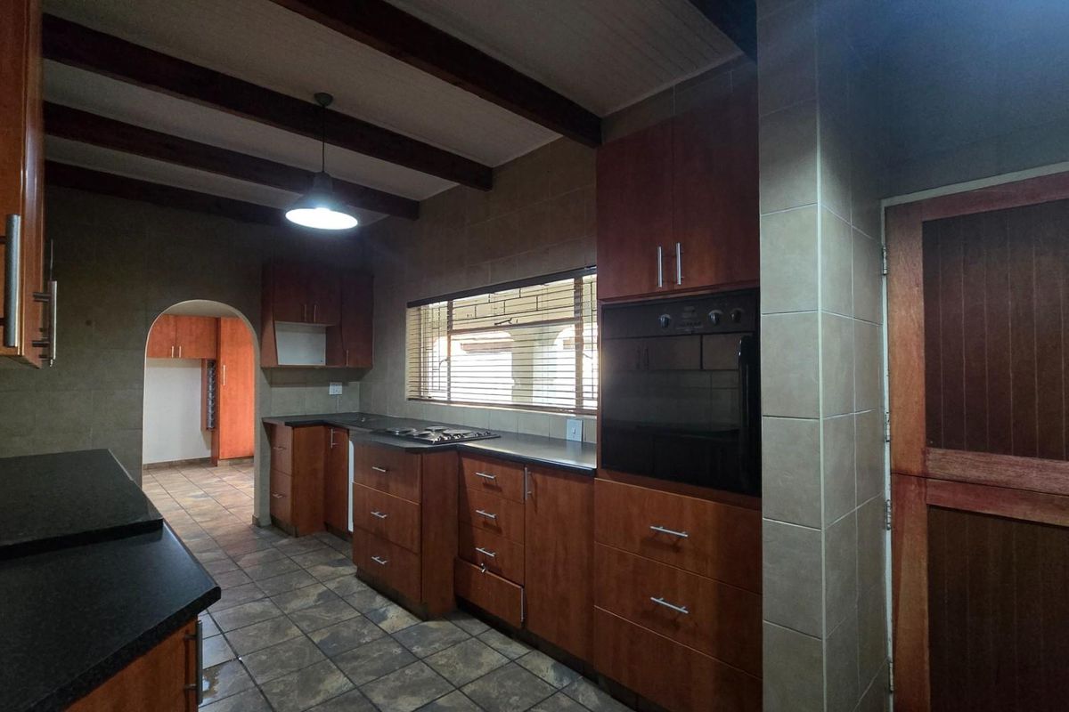 A functional kitchen featuring dark wood cabinetry, built-in oven, hob, tiled flooring, and exposed timber ceiling beams.
