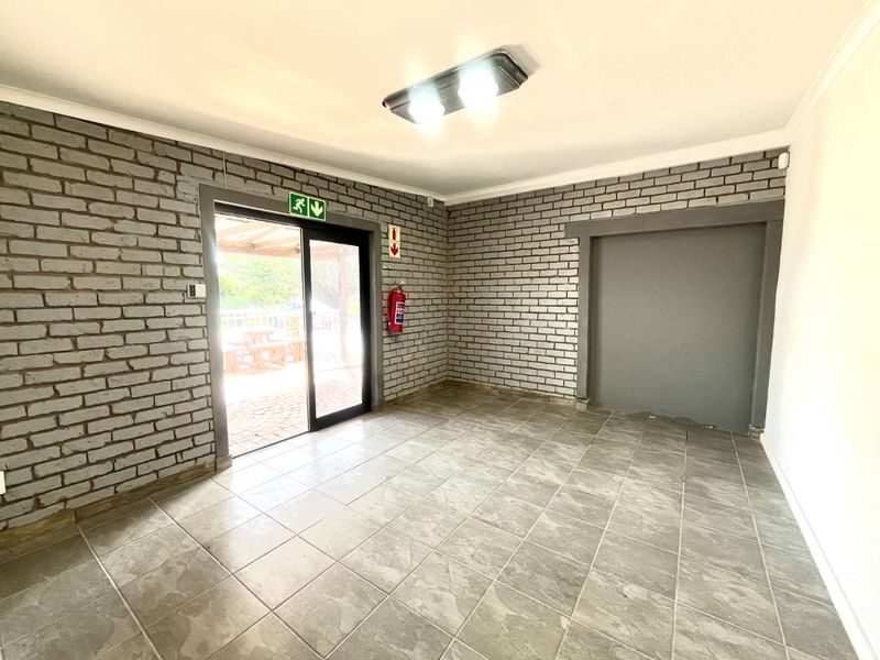 An empty, versatile room featuring exposed brick walls, tiled flooring, and a sliding glass door providing direct access to an outdoor area.