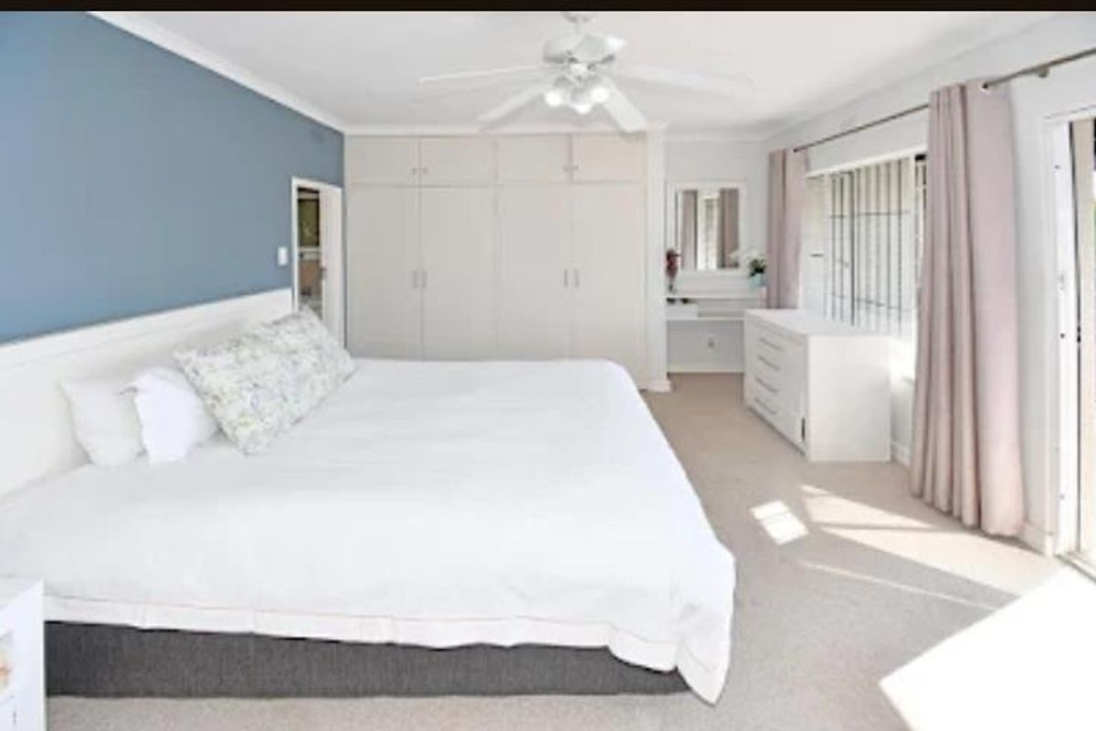 Spacious bedroom featuring built-in wardrobes, a ceiling fan, and large windows with security bars, offering a bright and functional living space.