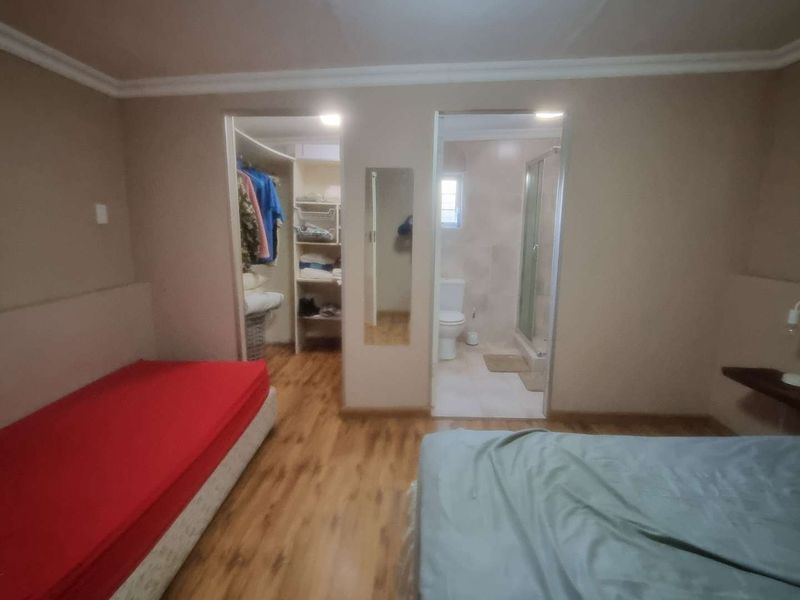 Bedroom featuring laminate flooring, an integrated walk-in closet, and an en-suite bathroom with a shower and toilet.