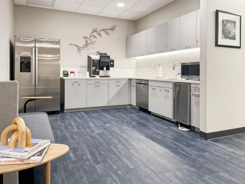 Modern office kitchenette featuring stainless steel appliances, sleek laminate cabinetry, under-cabinet lighting, and durable vinyl plank flooring.