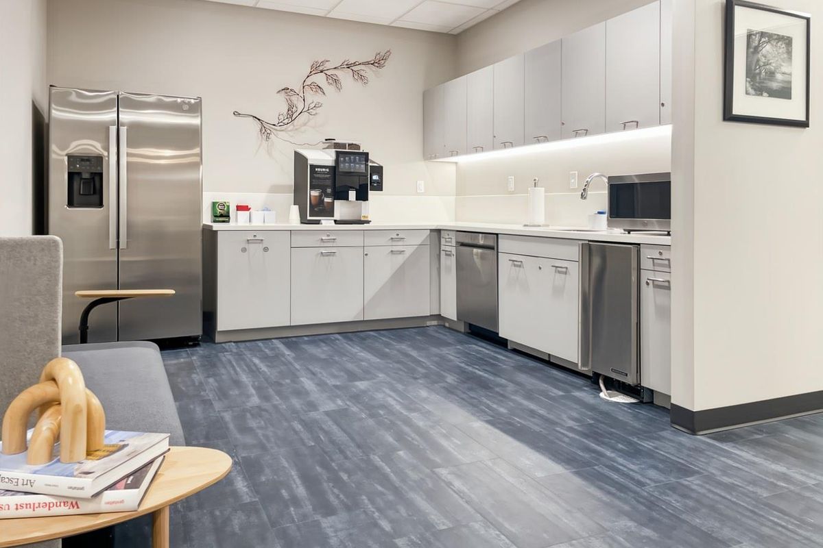Modern office kitchenette featuring stainless steel appliances, sleek laminate cabinetry, under-cabinet lighting, and durable vinyl plank flooring.