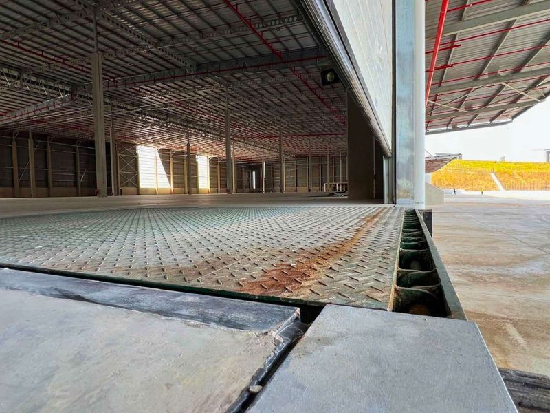 Large industrial warehouse interior featuring a dock leveller, exposed steel portal frame, and fire sprinkler system, suitable for logistics or manufacturing operations.