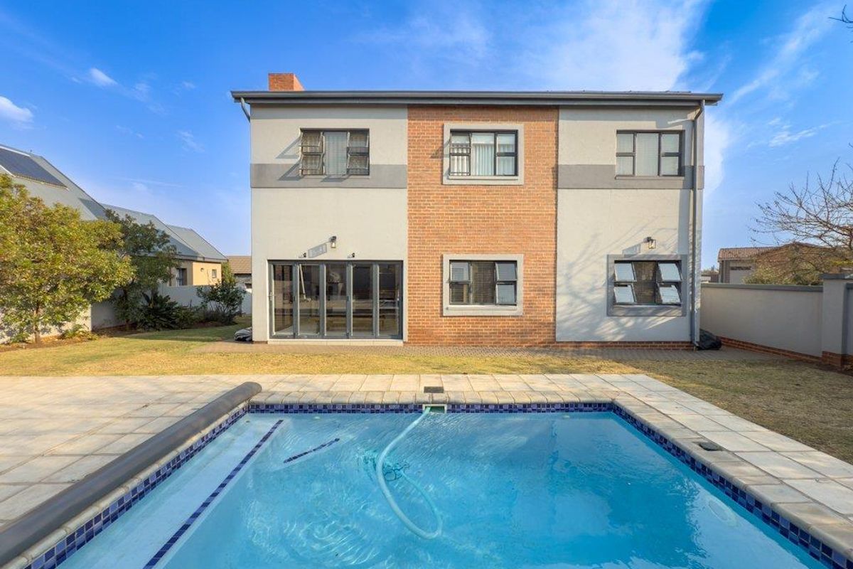 Rear view of a two-story house featuring a swimming pool, paved patio area, and a combination of brick and rendered facade finishes.
