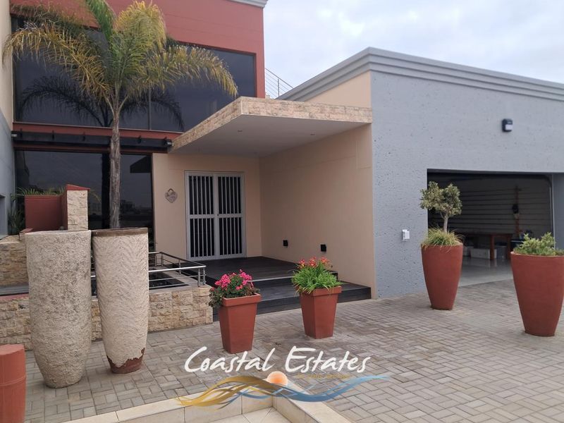 Modern front facade featuring stone cladding, a covered entrance with security gate, and a spacious double garage with paved driveway.