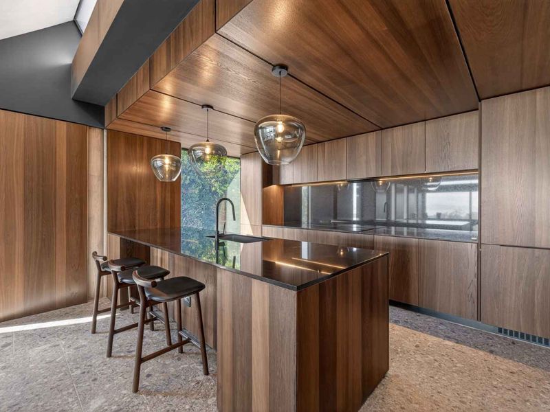 Modern luxury kitchen featuring high-end timber cabinetry, a sleek stone island with integrated sink, and sophisticated pendant lighting in a contemporary architectural space.
