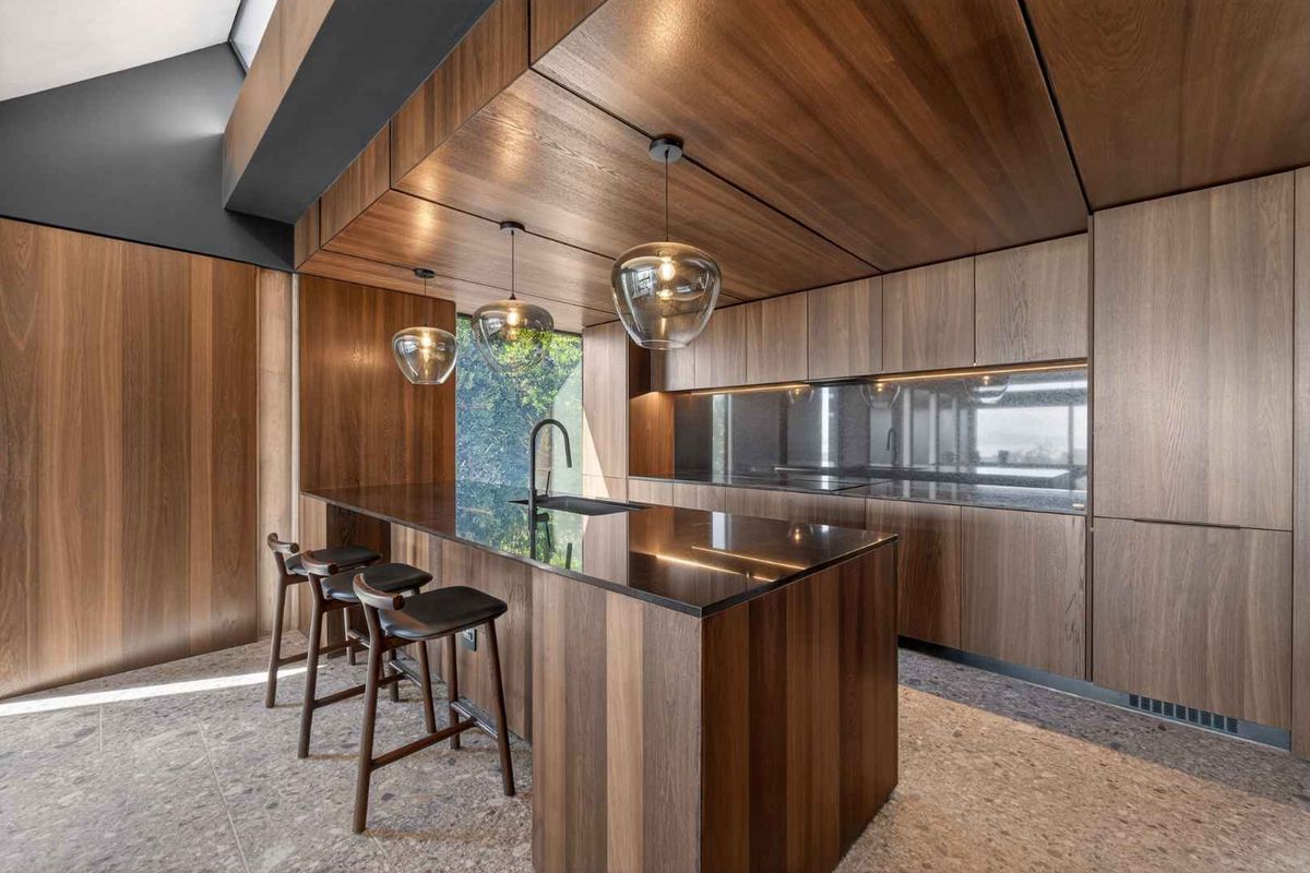 Modern luxury kitchen featuring high-end timber cabinetry, a sleek stone island with integrated sink, and sophisticated pendant lighting in a contemporary architectural space.