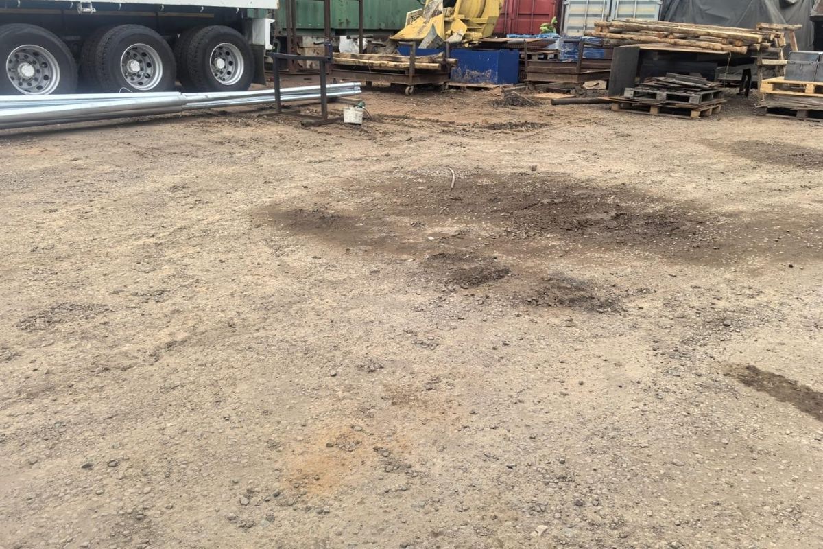 An unpaved industrial utility yard featuring uneven ground and storage space for heavy equipment and shipping containers.
