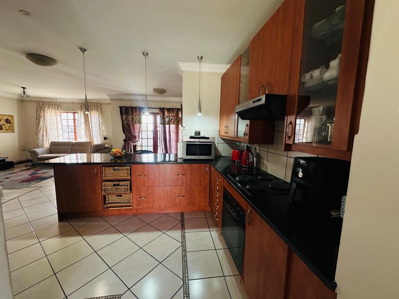 Open plan kitchen featuring wooden cabinetry, granite countertops, and integrated appliances, flowing into a spacious living area with tiled flooring throughout.