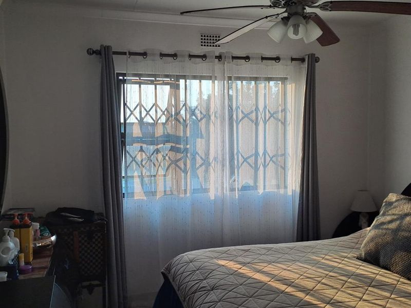 A bedroom featuring a ceiling fan, tiled flooring, and a window fitted with a security gate for added safety.