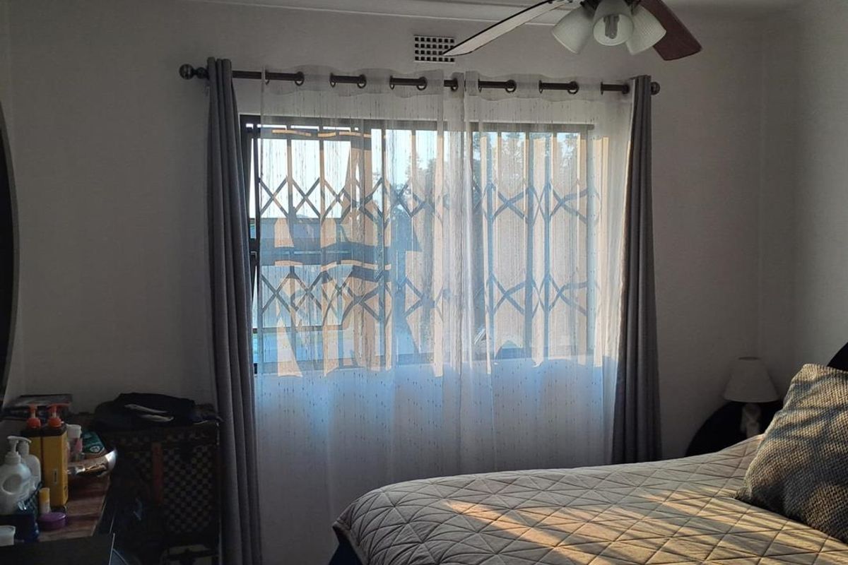 A bedroom featuring a ceiling fan, tiled flooring, and a window fitted with a security gate for added safety.