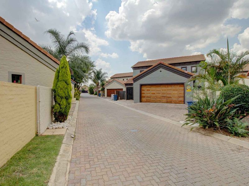 A view of the paved street within a residential townhouse complex, featuring well-maintained facades and garage access.