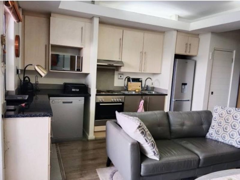Open-plan kitchen and living area featuring neutral cabinetry, laminate countertops, built-in oven, and durable laminate flooring in a functional apartment layout.