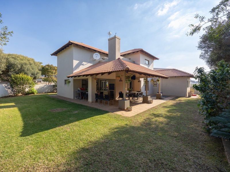 Rear view of the house featuring a spacious covered patio with a built-in braai, overlooking a well-maintained garden.