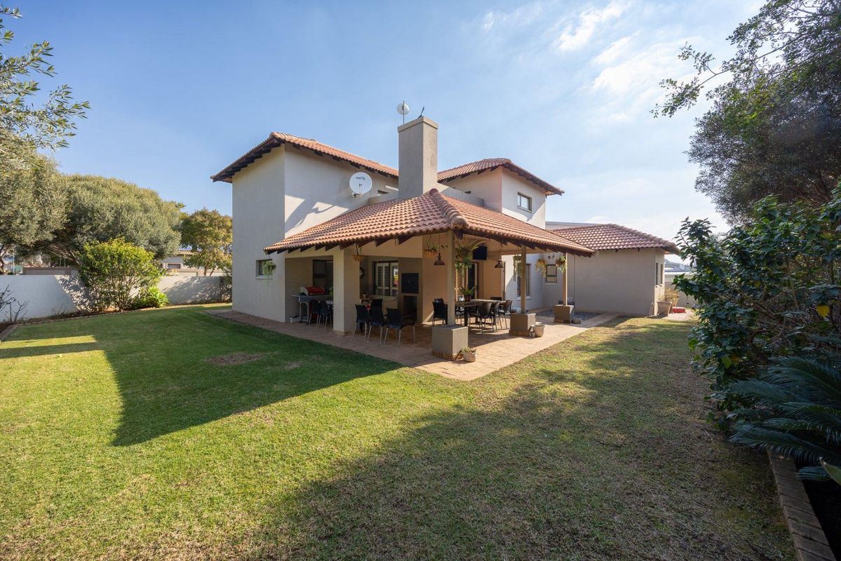 Rear view of the house featuring a spacious covered patio with a built-in braai, overlooking a well-maintained garden.