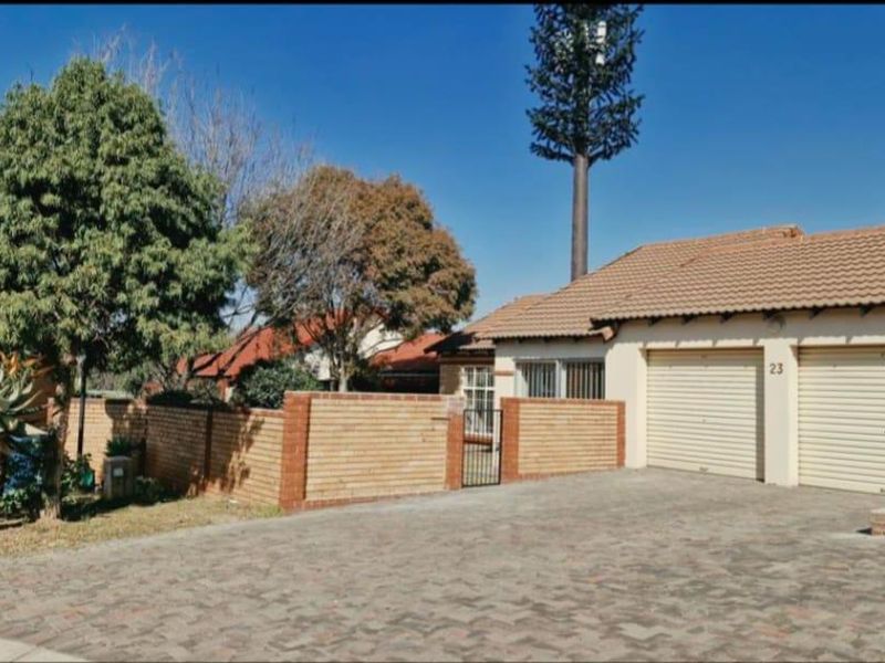 Front exterior view of a townhouse featuring a double garage, paved driveway, and brick boundary wall with a security gate.
