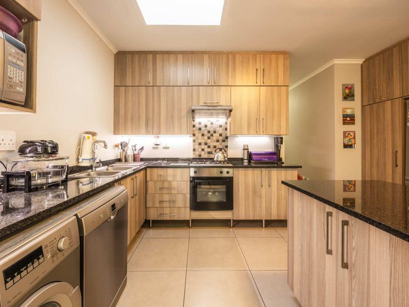 Modern kitchen featuring light wood cabinetry, granite countertops, built-in oven with gas hob, extractor fan, and a bright skylight.