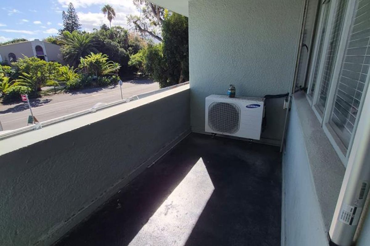 A covered balcony area featuring a wall-mounted air conditioning condenser unit and views of the surrounding neighborhood.