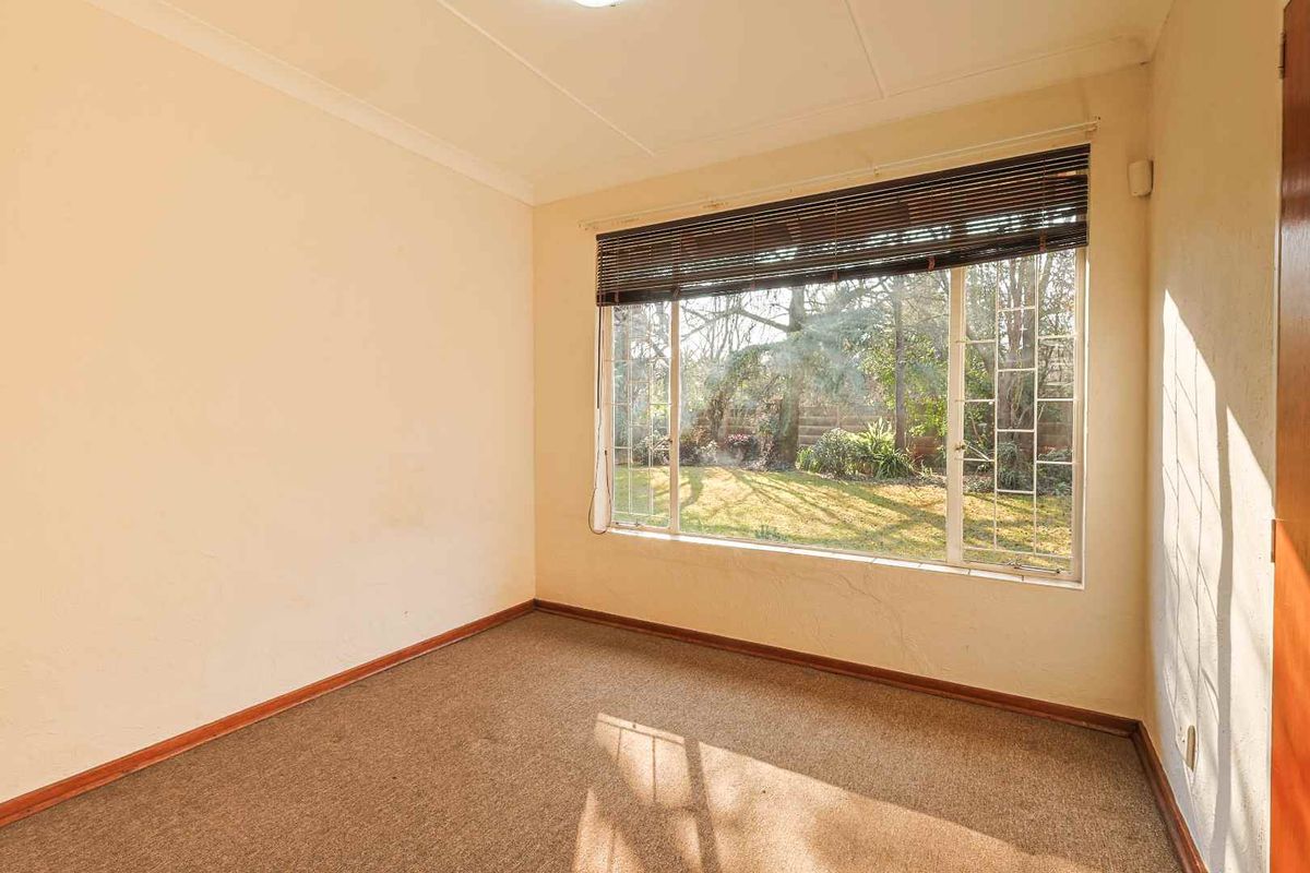 An empty bedroom featuring carpet flooring, coved ceilings, and a large window with blinds overlooking the garden.